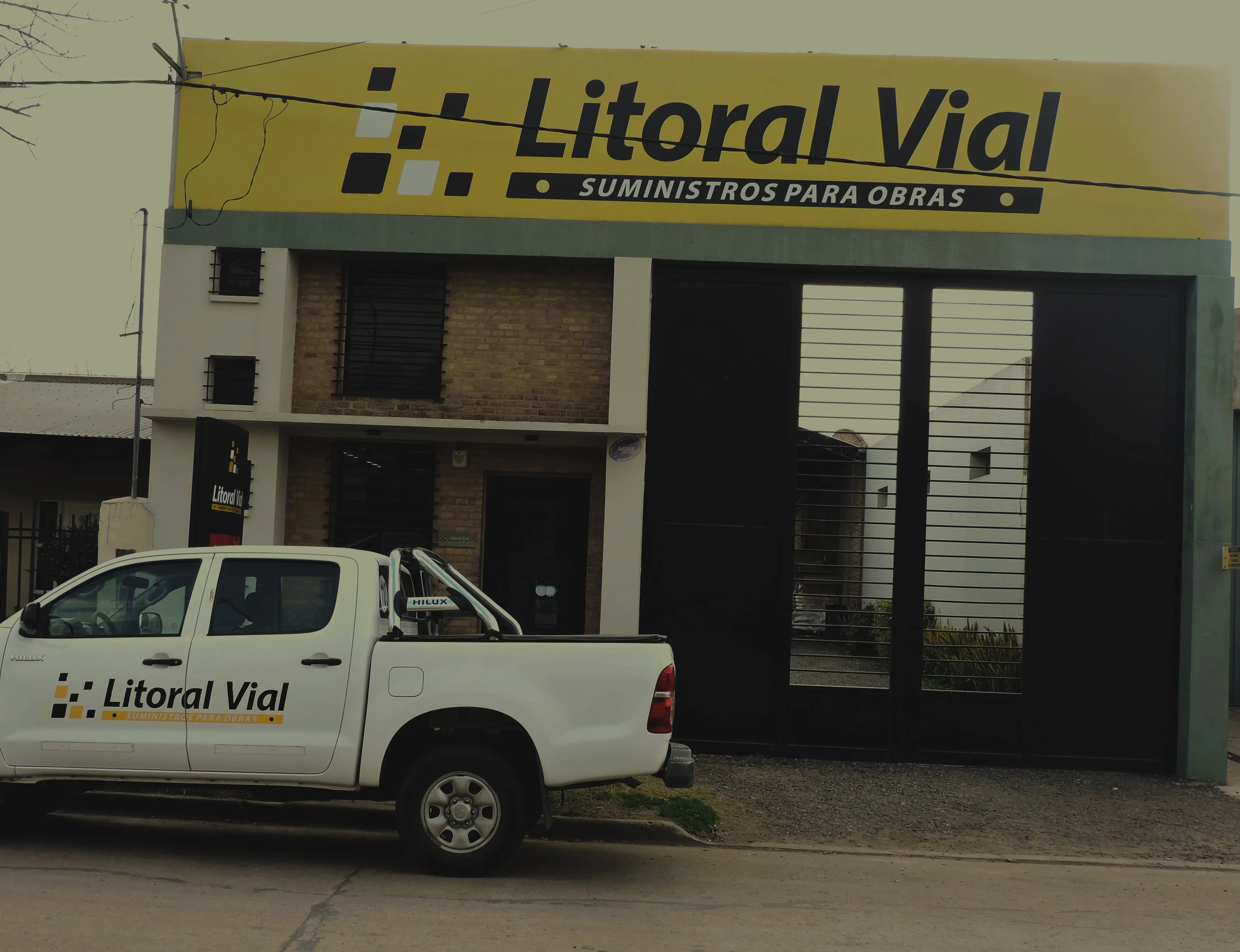 Sector de depósito con tambores de doscientos litros, rollos de membrana y baldes de productos Protex apilados sobre el piso de hormigón.