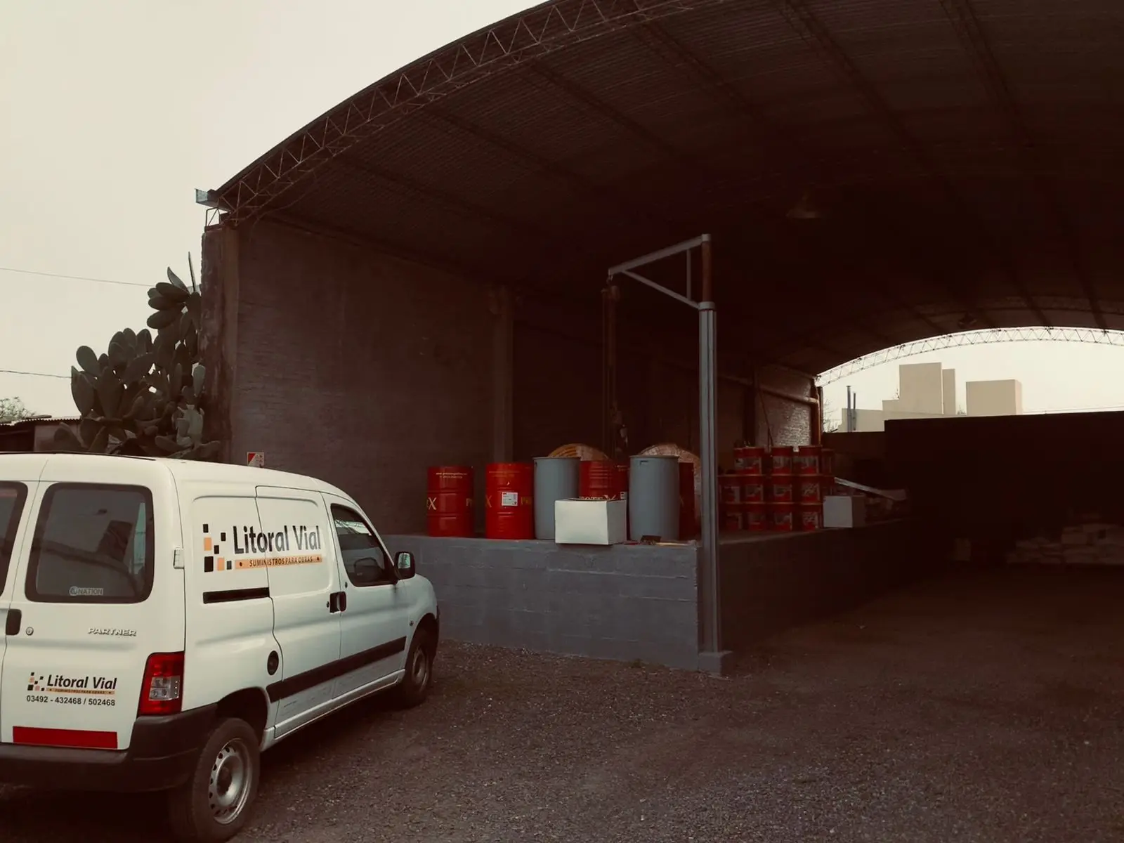 Playa de carga bajo tinglado: la camioneta de reparto de Litoral Vial junto a tambores y baldes de producto listos para despacho.
